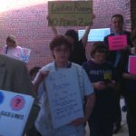 Supporters and opponents of adding gender identity to the Fairfax County Public Schools nondiscrimination policy hold competing signs outside of the school board meeting at Luther Jackson Middle School. (Photo credit: John Riley)